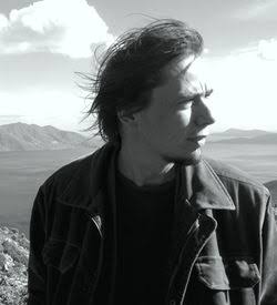 Black-and-white photo of Mirko in a jacket with the wind in his hair, looking out over a lake